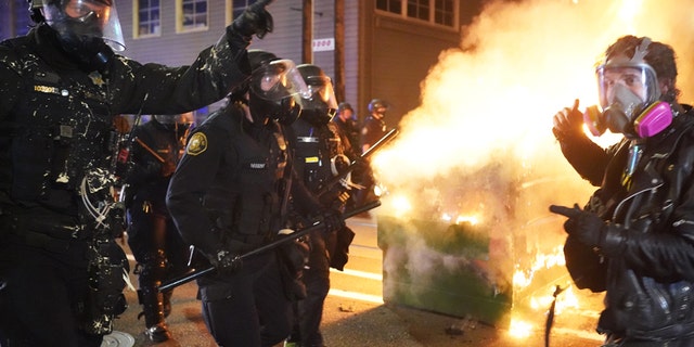 Portland police officers push protesters past a dumpster fire during a dispersal from in front of the Immigration and Customs Enforcement (ICE) detention facility in the early morning on August 21, 2020 in Portland, Oregon. (Photo by Nathan Howard/Getty Images)
