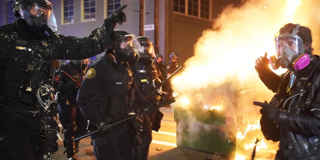 Portland police officers push protesters past a dumpster fire during a dispersal from in front of the Immigration and Customs Enforcement (ICE) detention facility in the early morning on August 21, 2020 in Portland, Oregon. (Photo by Nathan Howard/Getty Images)