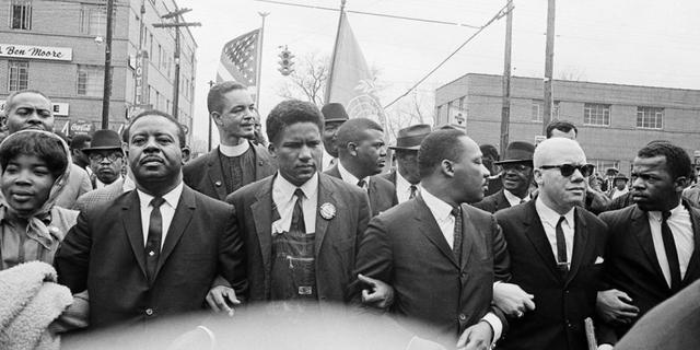 In this March 17, 1965, file photo, Dr. Martin Luther King Jr., fourth from left, foreground, locks arms with his aides as he leads a march of several thousands to the courthouse in Montgomery, Ala. From left are: an unidentified woman, Rev. Ralph Abernathy, James Foreman, King, Jesse Douglas Sr., and John Lewis.