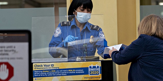 A Transportation Security Administration (TSA) agent wears a protective mask and stands behind a protective barrier. Photographer: Andrew Harrer/Bloomberg via Getty Images