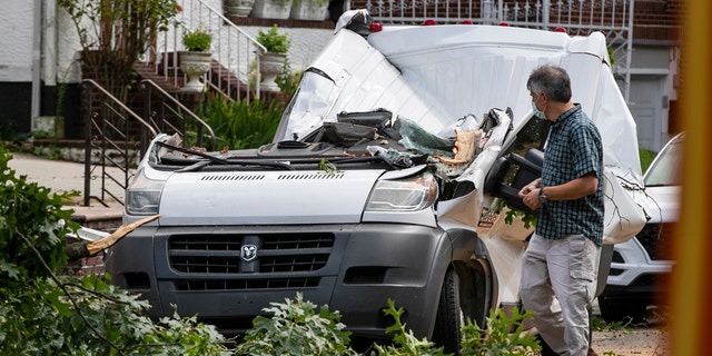 Officials observe a van where a person died from damage caused by a fallen tree as Tropical Storm Isaias moved past New York Tuesday, Aug. 4, 2020, in New York.