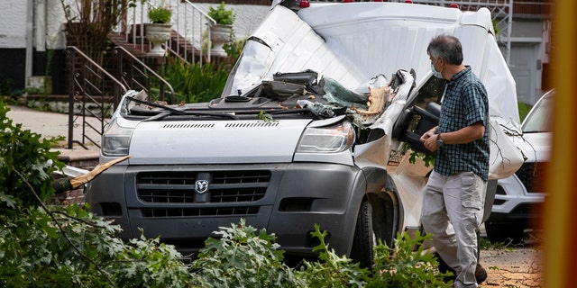 Officials observe a van where a person died from damage caused by a fallen tree as Tropical Storm Isaias moved past New York Tuesday, Aug. 4, 2020, in New York.