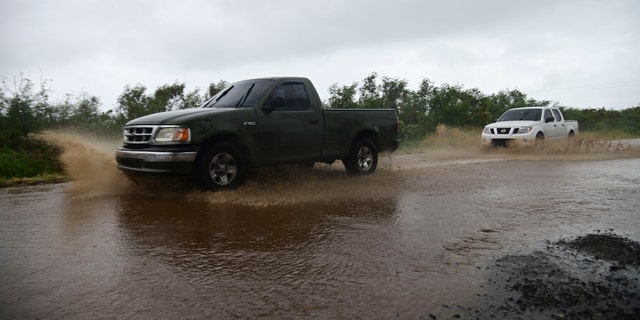 Vehicles drive through a flooded street caused by Tropical Storm Laura in Salinas, Puerto Rico, Saturday, Aug. 22, 2020. Laura began flinging rain across Puerto Rico and the Virgin Islands on Saturday morning and was expected to drench the Dominican Republic, Haiti and parts of Cuba during the day on its westward course.