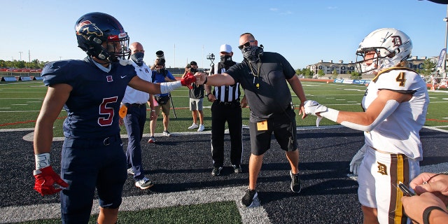 Davis High head coach Mitch Arquette, center, fist bumps Herriman High's Brock Hollingsworth (5) during the coin toss before the start of a high school football game on Thursday, Aug. 13, 2020, in Herriman, Utah. Utah is among the states going forward with high school football this fall. (AP Photo/Rick Bowmer)