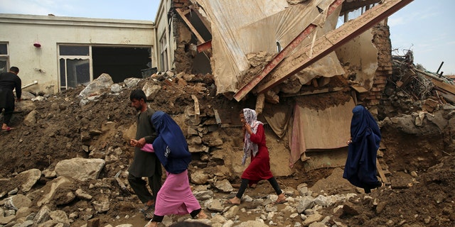 Afghan family walk near to the damaged houses after after a mudslide during heavy flooding in the Parwan province, north of Kabul, Afghanistan, Wednesday, Aug. 26, 2020.