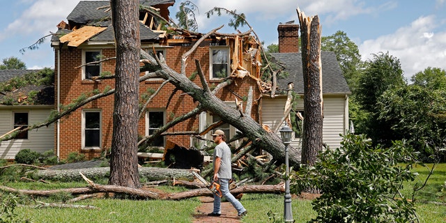 A man walks past a damaged house with a chainsaw in the Riverview neighborhood of Suffolk, Va., after Hurricane Isaias moved through the region Tuesday, August 4, 2020.