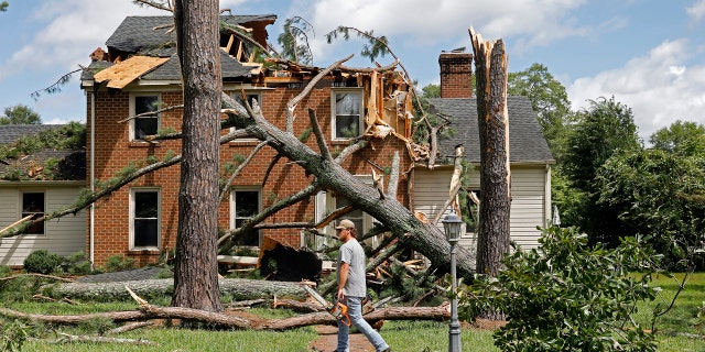 A man walks past a damaged house with a chainsaw in the Riverview neighborhood of Suffolk, Va., after Hurricane Isaias moved through the region Tuesday, August 4, 2020.