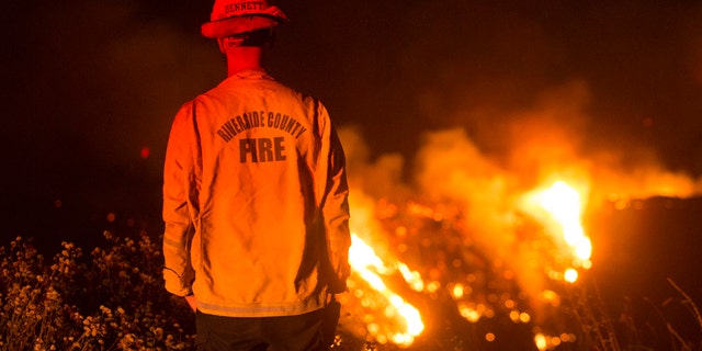A firefighter watches a brush fire at the Apple Fire in Banning, Calif., Saturday, Aug. 1, 2020.