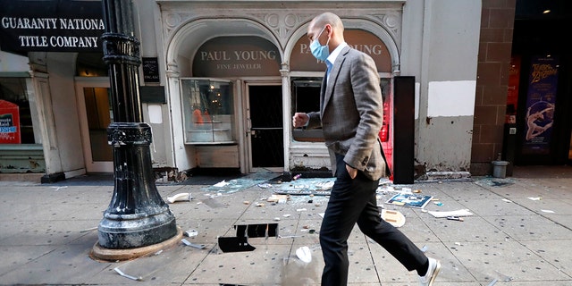 A pedestrian hops over debris Monday, Aug. 10, 2020, after a jewelry store was vandalized in Chicago's famed Loop. Chicago’s police commissioner says more than 100 people were arrested following a night of looting and unrest that left several officers injured and caused damage in the city’s upscale Magnificent Mile shopping district and other parts of the city. 