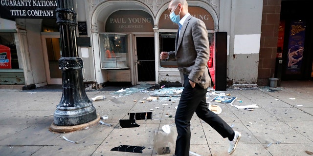 A pedestrian hops over debris Monday, Aug. 10, 2020, after a jewelry store was vandalized in Chicago's famed Loop. Chicago’s police commissioner says more than 100 people were arrested following a night of looting and unrest that left several officers injured and caused damage in the city’s upscale Magnificent Mile shopping district and other parts of the city.
