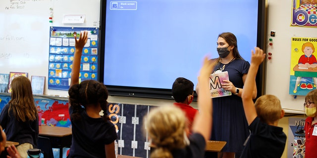 Students raise their hands while a teacher wears a protective mask during a lesson at a public charter school in Provo, Utah, U.S., on Thursday, Aug. 20, 2020. 