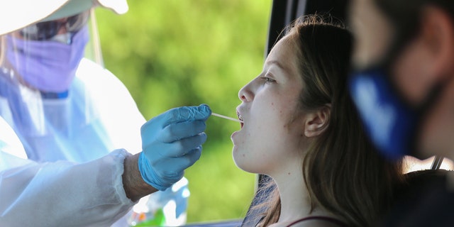 A health care worker gives a girl a throat swab test at a drive-in coronavirus (COVID-19) testing center at M.T.O. Shahmaghsoudi School of Islamic Sufism on Aug. 11, 2020, in Los Angeles, California. (Mario Tama/Getty Images)