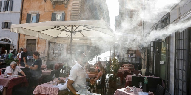 A fan sprays water as customers sit outside a cafe in downtown Rome, Friday, July 31, 2020.