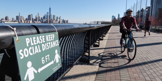 A cyclist rides past a newly installed sign encouraging social distancing to stop the spread of coronavirus along the Hudson River Walkway in Hoboken, N.J. (Photo by Gary Hershorn/Getty Images)