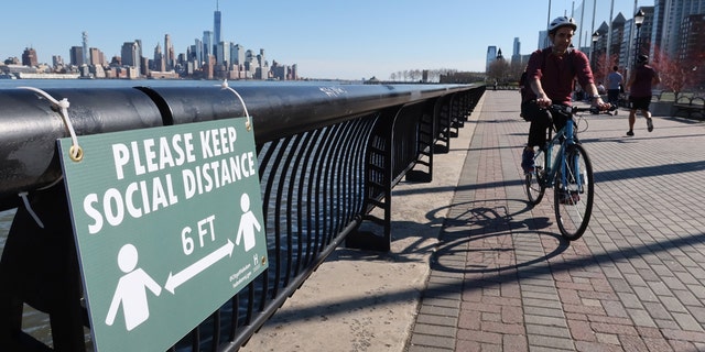 A cyclist rides past a newly installed sign encouraging social distancing to stop the spread of coronavirus along the Hudson River Walkway in Hoboken, N.J. (Photo by Gary Hershorn/Getty Images)