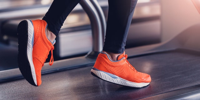 Comfortable sports shoes for running in the gym. Jogging shoes for running on a treadmill. Safety when performing exercises on cardio in sports shoes. Orange sports sneakers on the treadmill