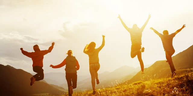A group of five happy friends are running and jumping in the sunset light against the background of mountains.Happiness and friendship concept
