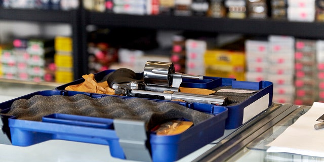 Revolver on a glass showcase displayed in a case with rows of ammunition in the background