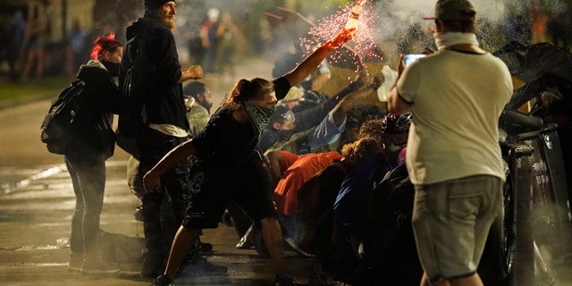 A protester tosses an object toward police during clashes outside the Kenosha County Courthouse late Tuesday, Aug. 25, 2020, in Kenosha, Wis., on third night of unrest following the shooting of a Black man, Jacob Blake, whose attorney said he was paralyzed after being shot multiple times by police. (AP Photo/David Goldman)