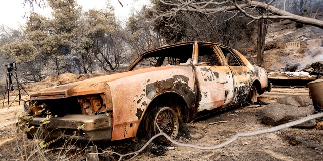 A burned vehicle rests along Pine Canyon Road as the Lake Fire burns in the Angeles National Forest. (AP)