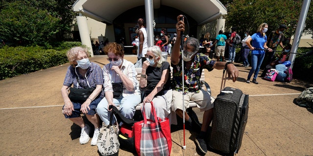 Evacuees, from right to left, Tommie McNeil, Elisabeth Pelham, Nota Norris, and a woman who did not want to be identified, wait to board a bus as they evacuate, Tuesday, Aug. 25, 2020, in Galveston, Texas.