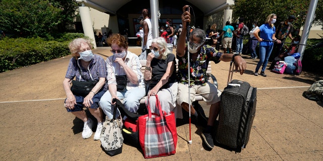 Evacuees, from right to left, Tommie McNeil, Elisabeth Pelham, Nota Norris, and a woman who did not want to be identified, wait to board a bus as they evacuate, Tuesday, Aug. 25, 2020, in Galveston, Texas.