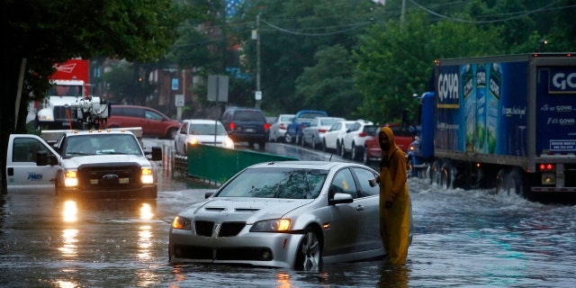 A man checks on a stranded vehicle during Tropical Storm Isaias, Tuesday, Aug. 4, 2020, in Philadelphia. The storm spawned tornadoes and dumped rain during an inland march up the U.S. East Coast after making landfall as a hurricane along the North Carolina coast. (AP Photo/Matt Slocum)