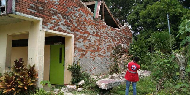 In this handout photo provided by the Philippine Red Cross, a volunteer takes photos of a damaged structure after a strong earthquake struck in Cataingan, Masbate province, central Philippines on Tuesday Aug. 18, 2020.
