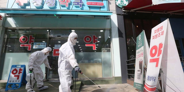Workers disinfect as a precaution against the coronavirus in front of a pharmacy in Goyang, South Korea, Tuesday, Aug. 25, 2020. South Korea is closing schools and switching back to remote learning in the greater capital area as the country counted its 12th straight day of triple-digit daily increases in coronavirus cases. (AP Photo/Ahn Young-joon)