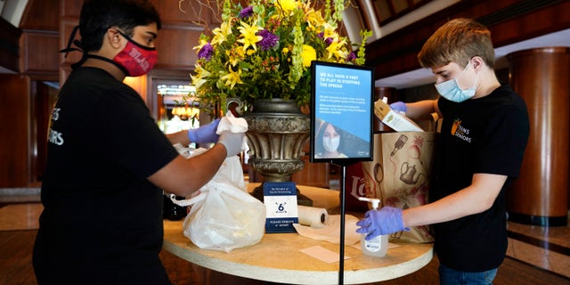 Dhruv Pai, 16, left, and Matthew Casertano, 15, both of North Potomac, Md., wipe down groceries with disinfectant as they deliver them to David Benkin, 85, and Rebecca Adler, 81, Wednesday Aug. 19, 2020, in North Bethesda, Md., as part of the nonprofit organization, "Teens Helping Seniors" that Pai and Casertano co-founded. The teens call when they are outside and leave the bags of groceries on a table in the lobby of the building for the seniors to pick up after they leave, in order to minimize the risk of coronavirus exposure for the seniors.