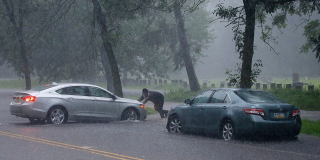 A man pushes a car through a flooded street during Tropical Storm Isaias, Aug. 4, in Philadelphia.