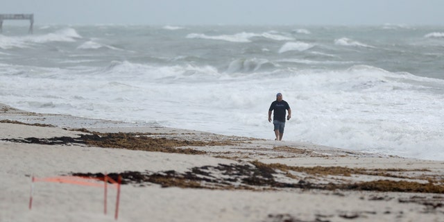 A beach goer walks along the shore as waves churned up by Tropical Storm Isaias crash near Jaycee Beach Park, Sunday, Aug. 2, 2020, in Vero Beach, Fla.
