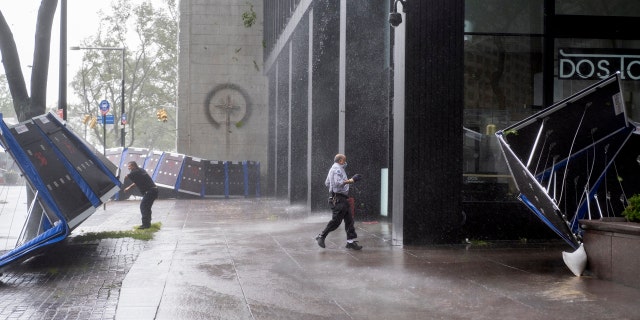 People try to secure barriers meant to block flood waters that were picked up by the wind at a building at Water and State Streets in lower Manhattan Tuesday, Aug 4, 2020.