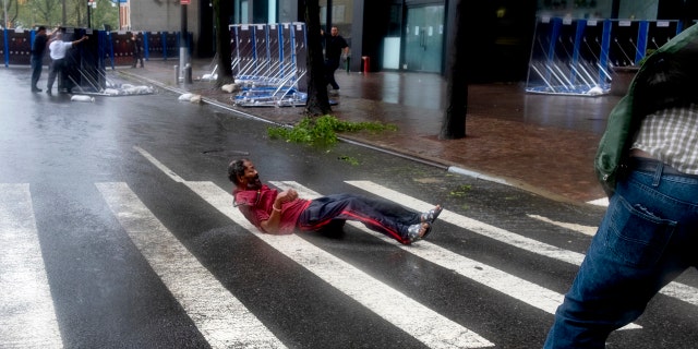 A person lays on a crosswalk after being knocked to the street by wind in lower Manhattan Tuesday, Aug. 4, 2020, as Tropical Storm Isaias produced strong winds as the storm moved past, at times causing damage.