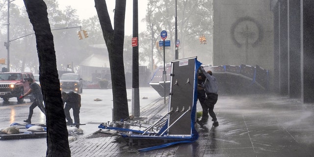People try to secure barriers meant to block flood waters that were picked up by the wind at a building at Water and State Streets in lower Manhattan Tuesday, Aug 4, 2020, as winds from Tropical Storm Isaias piked them up and tossed them about.