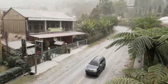 A car drives on a road covered with volcanic ash from the eruption of Mount Sinabung, in Karo, North Sumatra, Indonesia, Monday, Aug. 10, 2020.