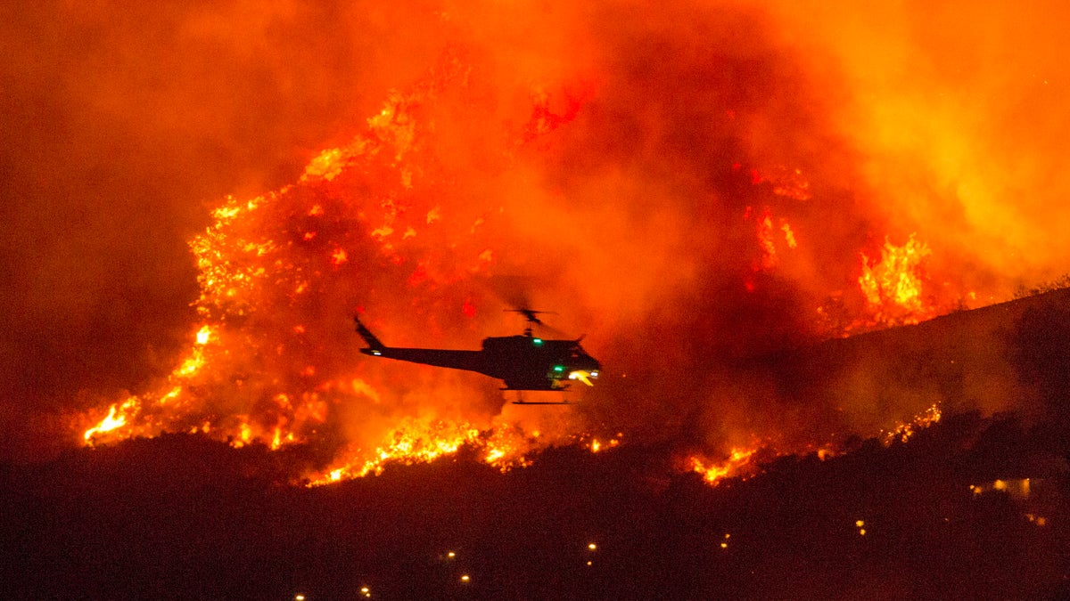 FILE - In this Saturday, Sept. 5, 2020, file photo, a helicopter prepares to drop water at a wildfire in Yucaipa, Calif. A couple’s plan to reveal their baby’s gender at a party went up in smoke Saturday at El Rancho Dorado Park in Yucaipa, when a pyrotechnical device they used sparked a wildfire that has burned thousands of acres. (AP Photo/Ringo H.W. Chiu, File)
