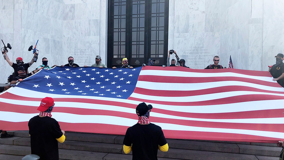 Right-wing protesters unfurl a flag on the steps of Oregon State Capitol for a pro-Donald Trump rally at the Capitol in Salem, Ore. on Monday, Sept. 7, 2020. (AP Photo/Andrew Selsky)
