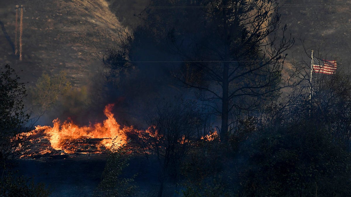 An American flag waves in the the wind next to a pile of burning railroad ties in the wake of the Cold Springs Canyon Pearl Hill Fire, Monday, Sept. 7, 2020, in Okanogan, Wash. (Associated Press)