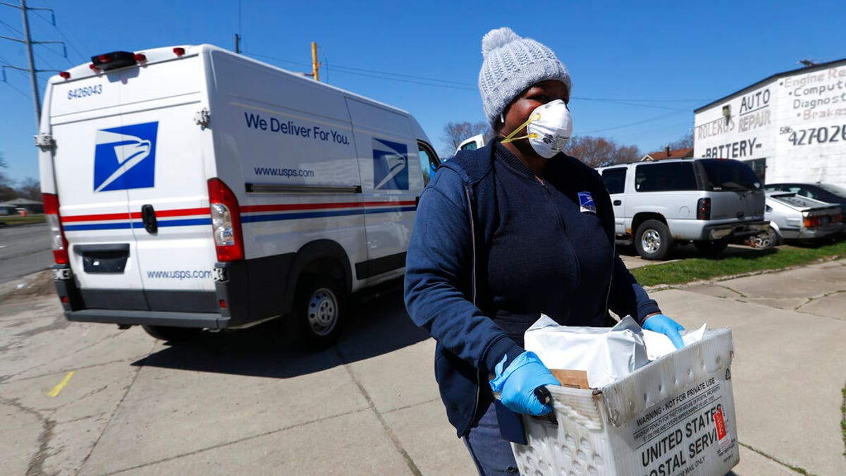 FILE: A United States Postal Service worker makes a delivery with gloves and a mask in Warren, Mich. 