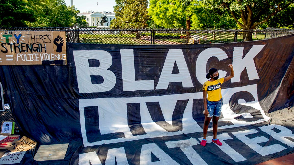 The White House is visible behind a woman who holds her fist up as she poses for a photograph with a large banner that reads Black Lives Matter hanging on a security fence in Washington, after days of protests over the death of George Floyd.