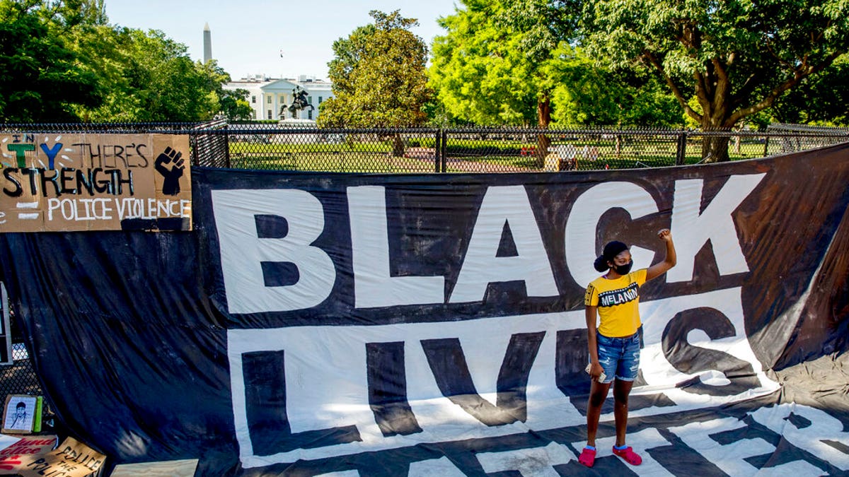 FILE: The White House is visible behind a woman who holds her fist up as she poses for a photograph with a large banner that reads Black Lives Matter hanging on a security fence in Washington, after days of protests over the death of George Floyd.?