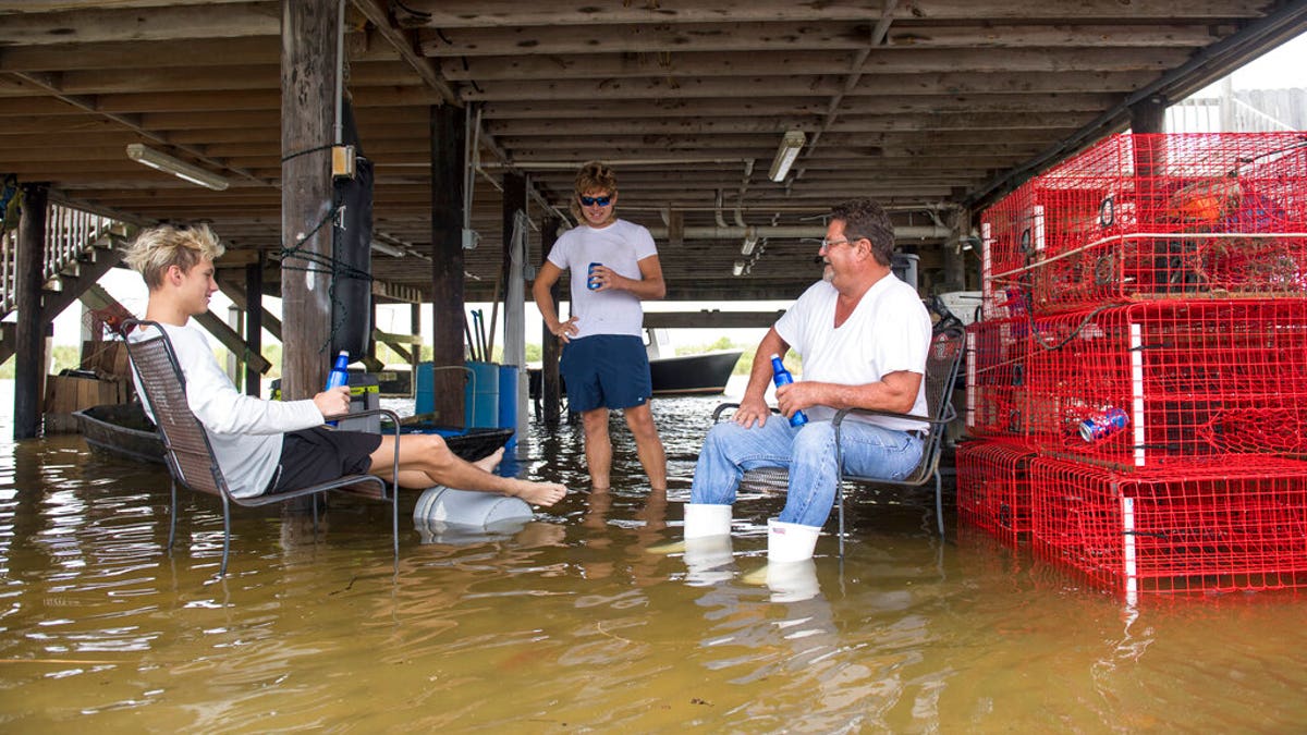 Hanging out in flood waters, Cameron Fogg, right, sits by his crab traps as he drinks a beer with Austin Claiborne, 18, left, and Cameron Gomez, center, in Salt Bayou near Slidell, La., on Tuesday, September 15, 2020. Hurricane Sally missed Louisiana, but its effect, such as high water, could be felt along the region. Fogg has lived in this house for 30 years and he said he's getting tired of the recurrence of rising water. (Chris Granger/The Advocate via AP)