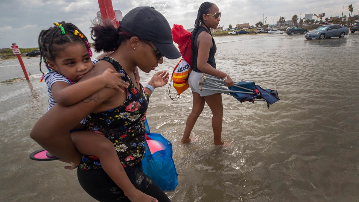 Stacey Young gives her daughter, Kylee Potts, a piggyback ride across the flooding Stewart Beach parking lot in Galveston, Texas on Saturday, Sept. 19, 2020.