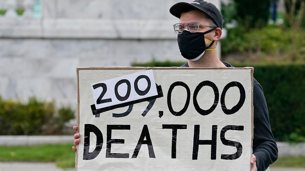 A man holds up a sign on the coronavirus deaths in America at a rally near the debate hall, Tuesday, Sept. 29, 2020, in Cleveland. The first presidential debate between Republican candidate President Donald Trump and Democratic candidate and former Vice President Joe Biden is being held in Cleveland Tuesday. (AP Photo/Tony Dejak)