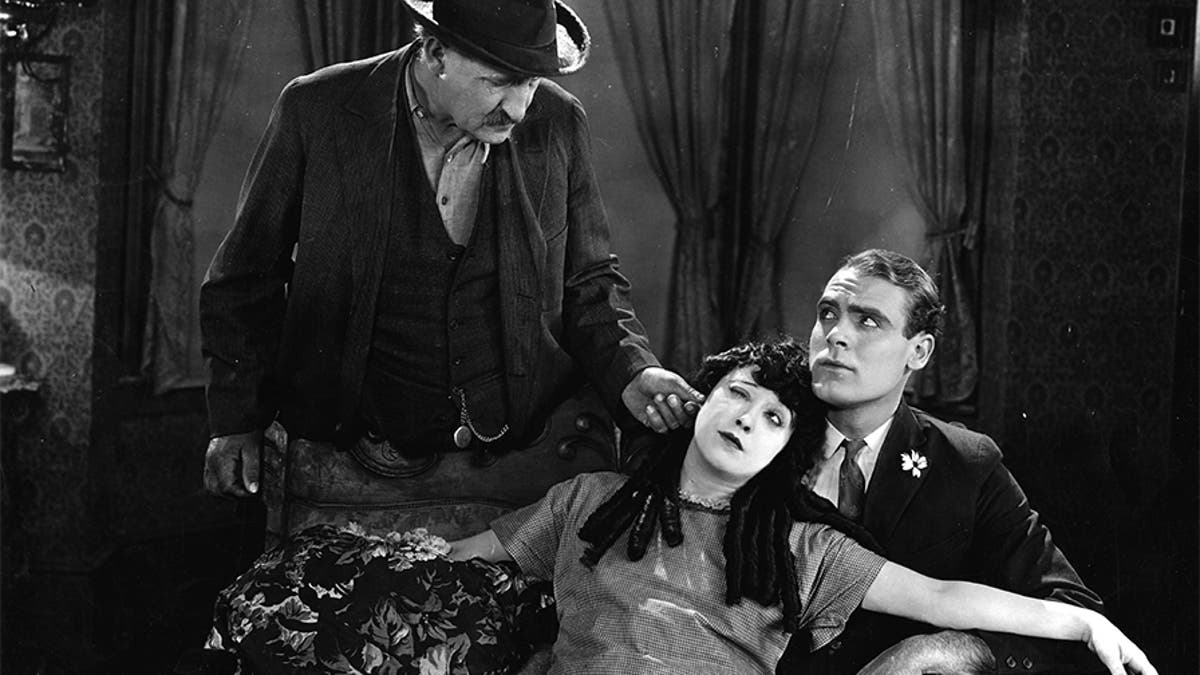 Actress Mabel Normand (1894-1930) gets her ear pulled by a possessive father in this scene from the 1923 film 'The Extra Girl'. Ralph Graves (1901-1977) sits next to her on the sofa. 