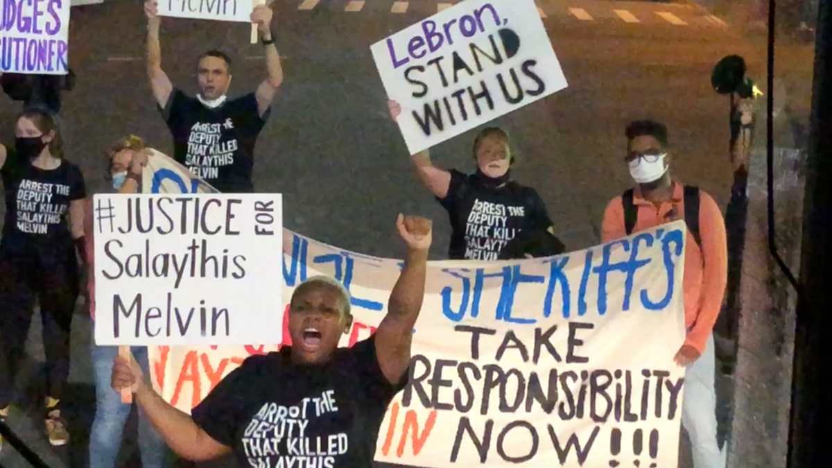 A small number of protesters of the August shooting in Central Florida of a Black man, Salaythis Melvin, hold signs and shout into megaphones, briefly blocking a bus chartered by the NBA from entering the Walt Disney World campus in Lake Buena Vista, Fla., Saturday night, Sept. 12, 2020, with the group saying it wanted LeBron James, Russell Westbrook and other top players to take notice. (AP Photo/Tim Reynolds)