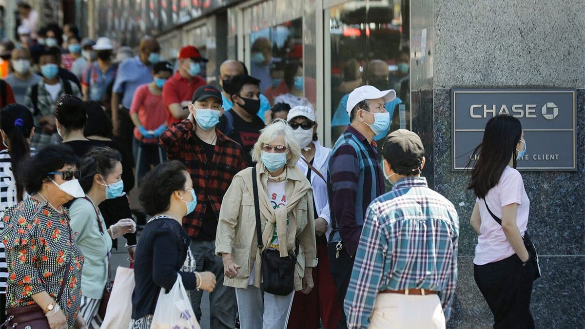 Patrons wearing protective masks wait to enter a Chase bank location, Monday, June 8, 2020, in the Flushing section of the Queens borough of New York. After three bleak months, New York City will try to turn a page when it begins reopening Monday after getting hit first by the coronavirus, then an outpouring of rage over racism and police brutality. (AP Photo/Frank Franklin II)