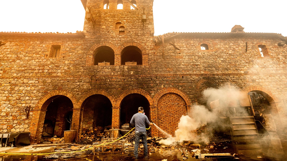 Cellar worker Jose Juan Perez sprays water on burning debris at Castello di Amorosa, Monday, Sept. 28, 2020, in Calistoga, Calif., which was damaged in the Glass Fire.