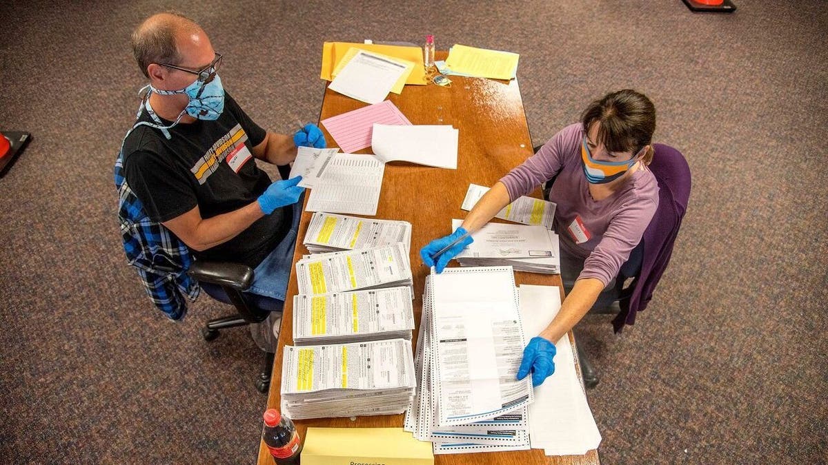 In this photo provided by Wisconsin Watch, election workers Jeff and Lori Lutzka, right, process absentee ballots at Milwaukee's central count facility on Aug. 11, 2020. Wisconsin elections officials are taking multiple steps to make mail-in voting smoother in November, when most people are expected to vote absentee. (Will Cioci/Wisconsin Watch via AP)